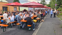 Besucher des Weinfestes Sitzen zusammen auf Bierbänken.