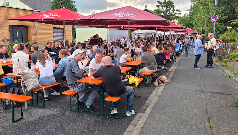Besucher des Weinfestes Sitzen zusammen auf Bierbänken.